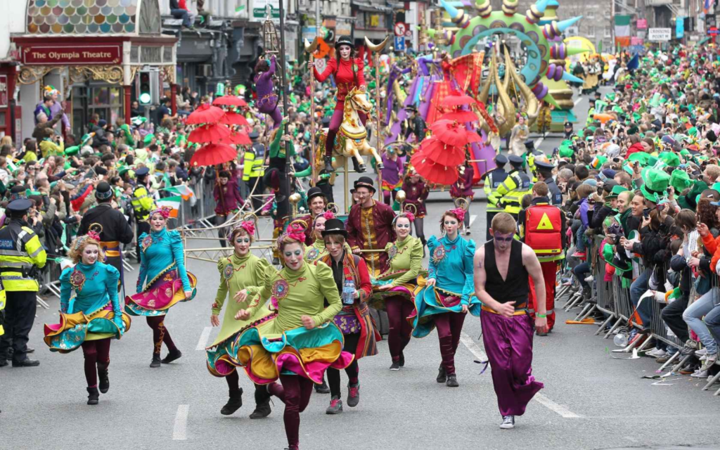 carnival watching the dancers in center wearing red hair,green shirt with miniskirt in black pants and horse riders at the back
